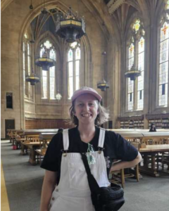 Lilli stands in the cathedral-style main hall of the University of Washington. She wears a pink hat and white overalls.