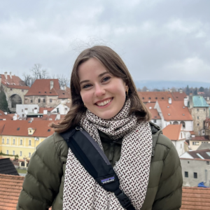 Article author Grace smiles in a puffy coat from a European rooftop.